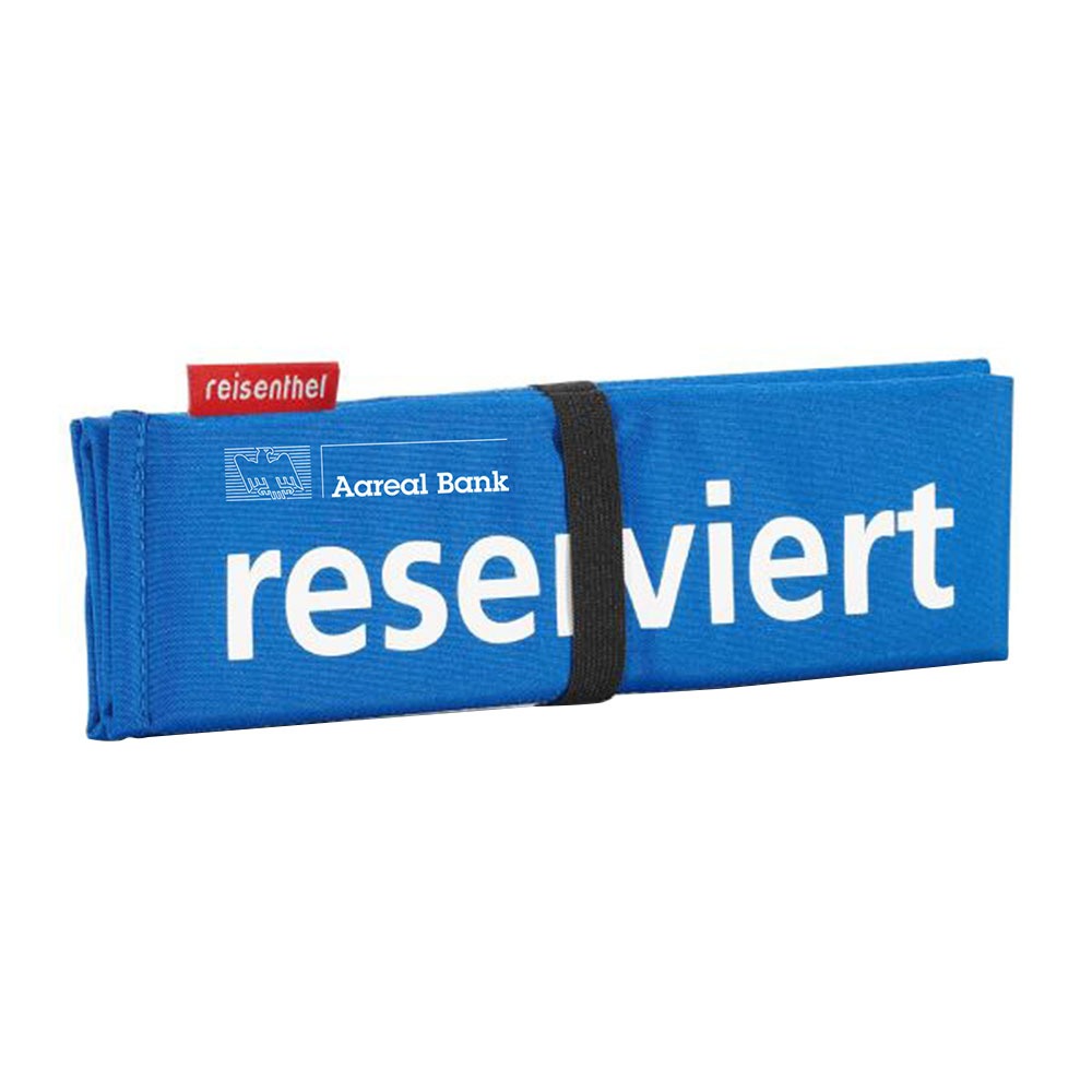 Ein blaues, gefaltetes Stoffschild mit schwarzem Gummiband und weißem Text „Reserviert“. Auf einem roten Schild steht „reisenthel“, und das Logo der Vollblut Aareal Bank ist in Weiß auf den Stoff gedruckt.